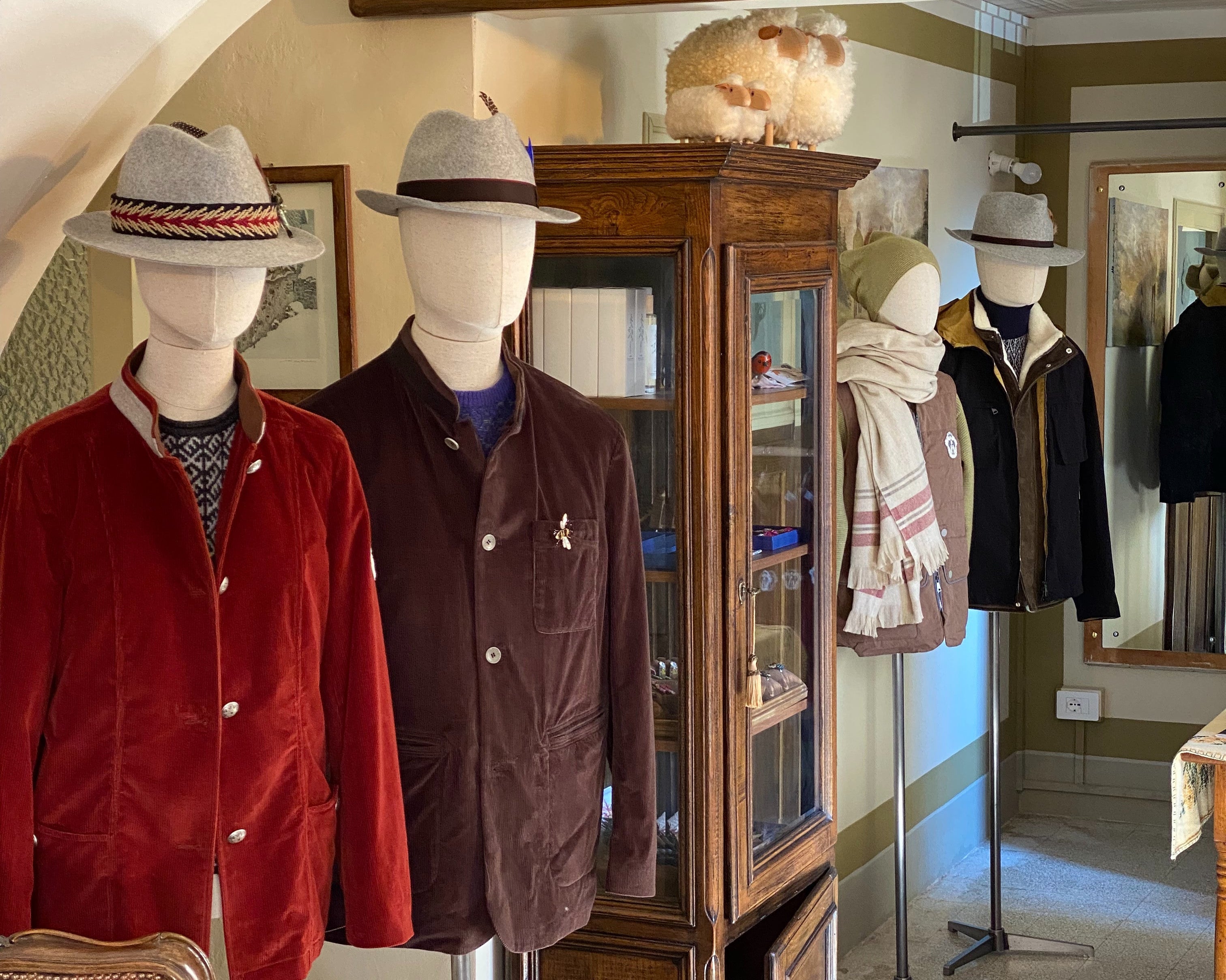 Mannequins dressed in winter clothing with a wooden cabinet in a store setting.