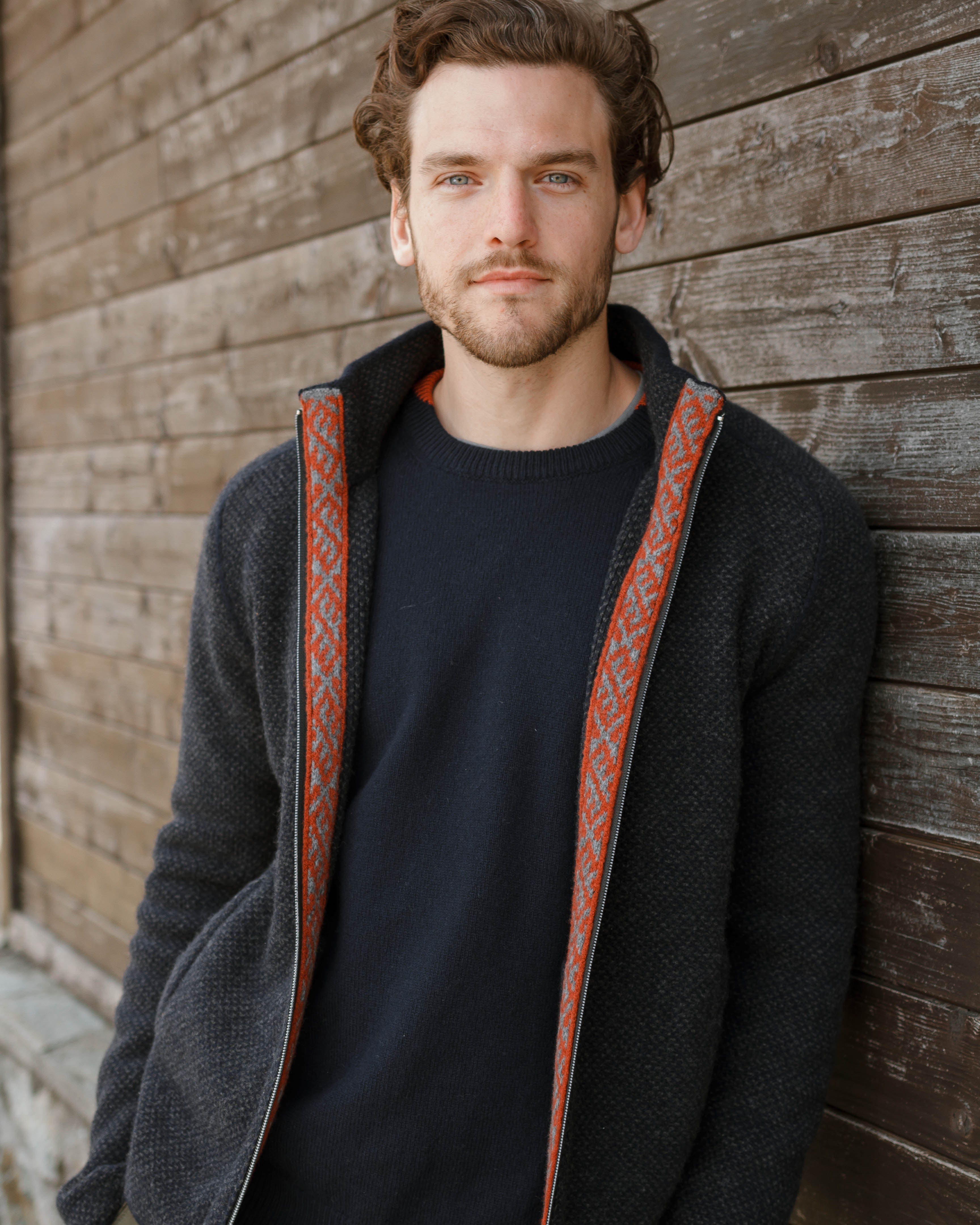 Man wearing a dark jacket with red lining against a wooden wall