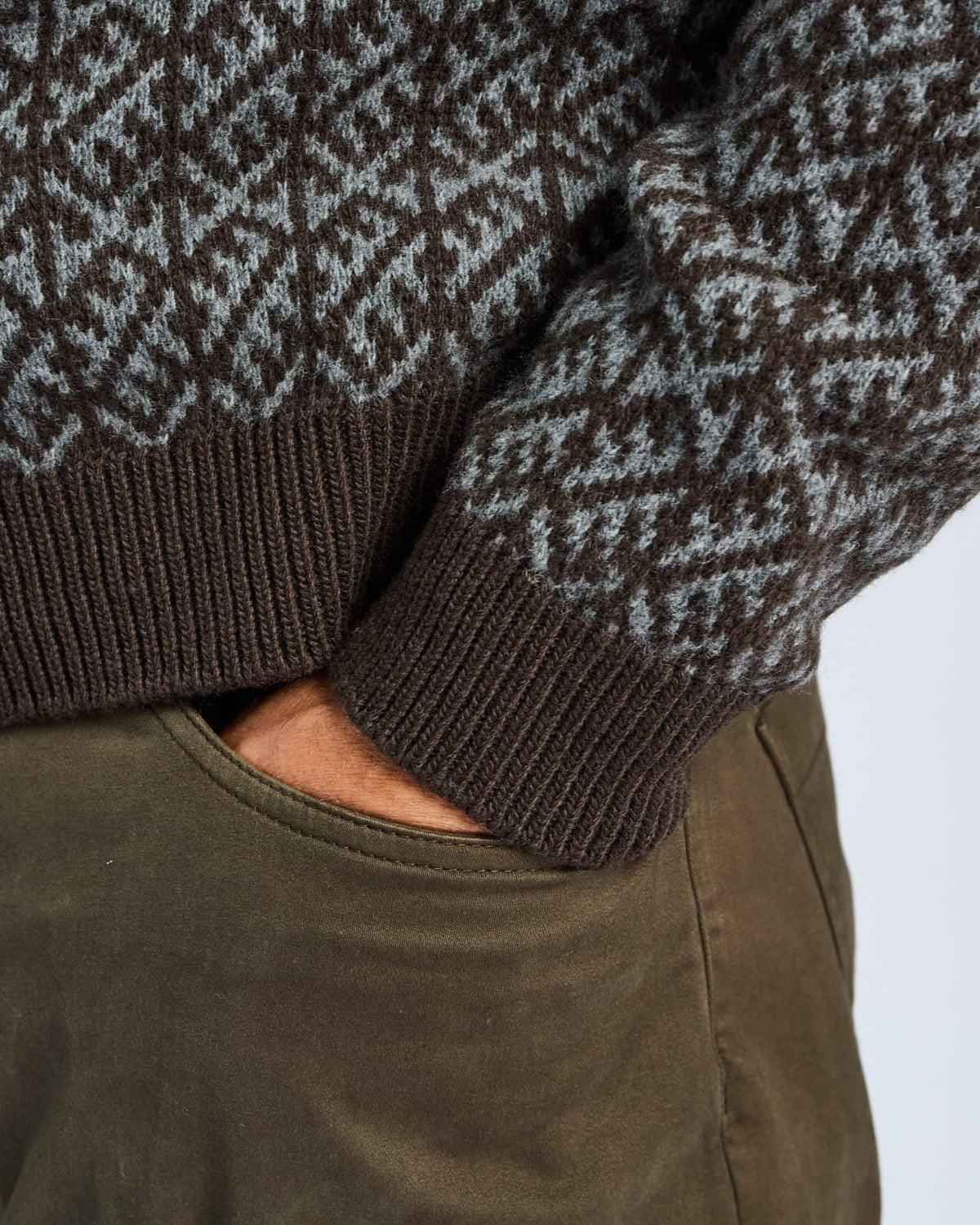 Close-up of a person wearing a patterned sweater and green pants on a white background