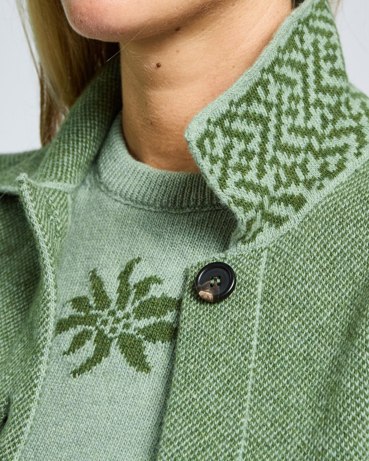 Close-up of a green knitted cardigan with patterned collar and button detail.