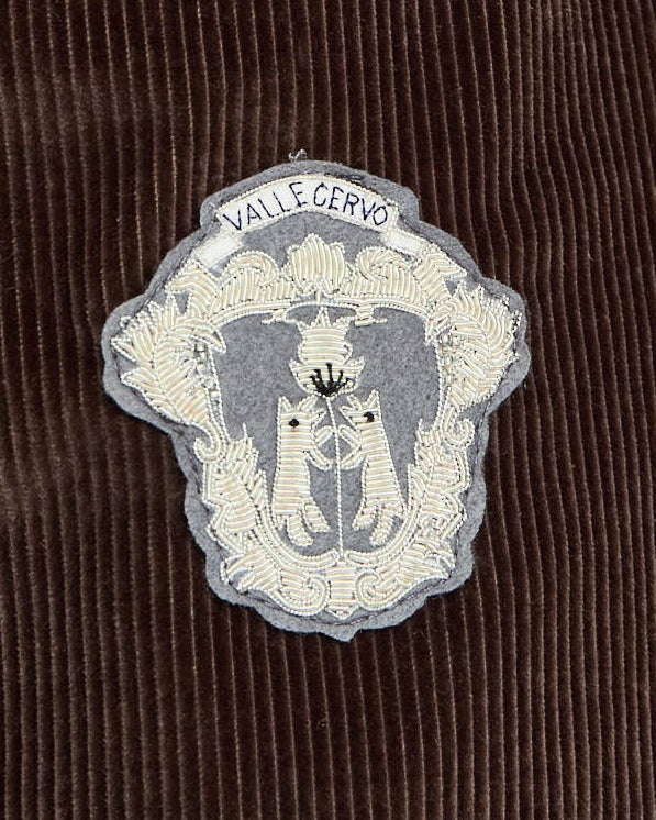 Brown corduroy jacket with a decorative patch on a light gray background