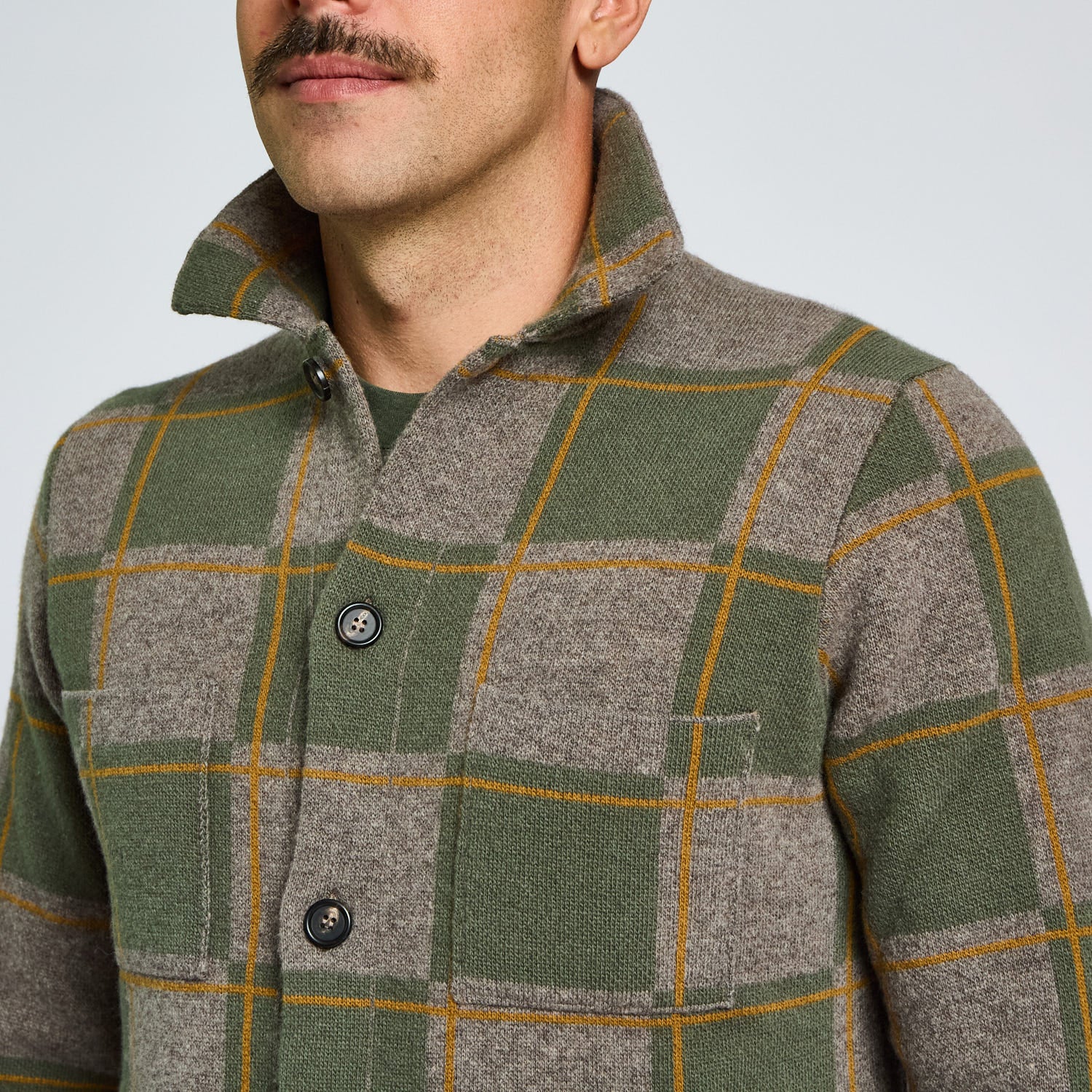 Man wearing a green and gray checkered jacket against a light background
