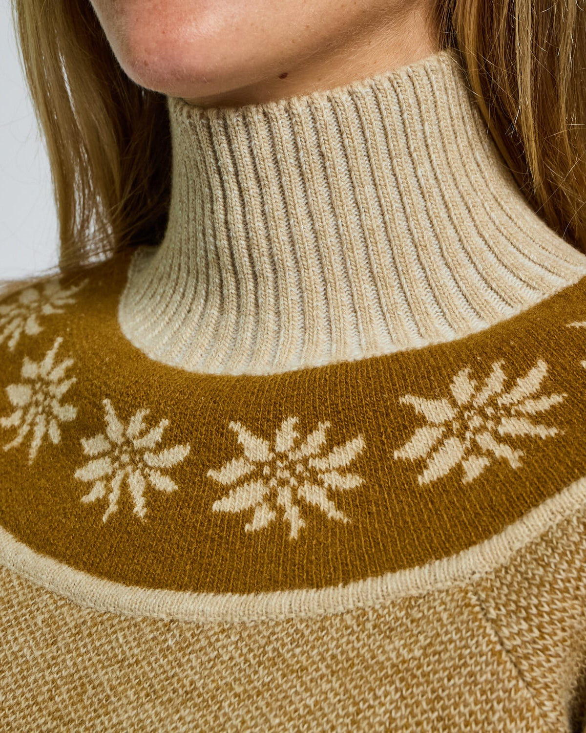 Close-up of a beige sweater with brown neckline featuring floral patterns on a plain background