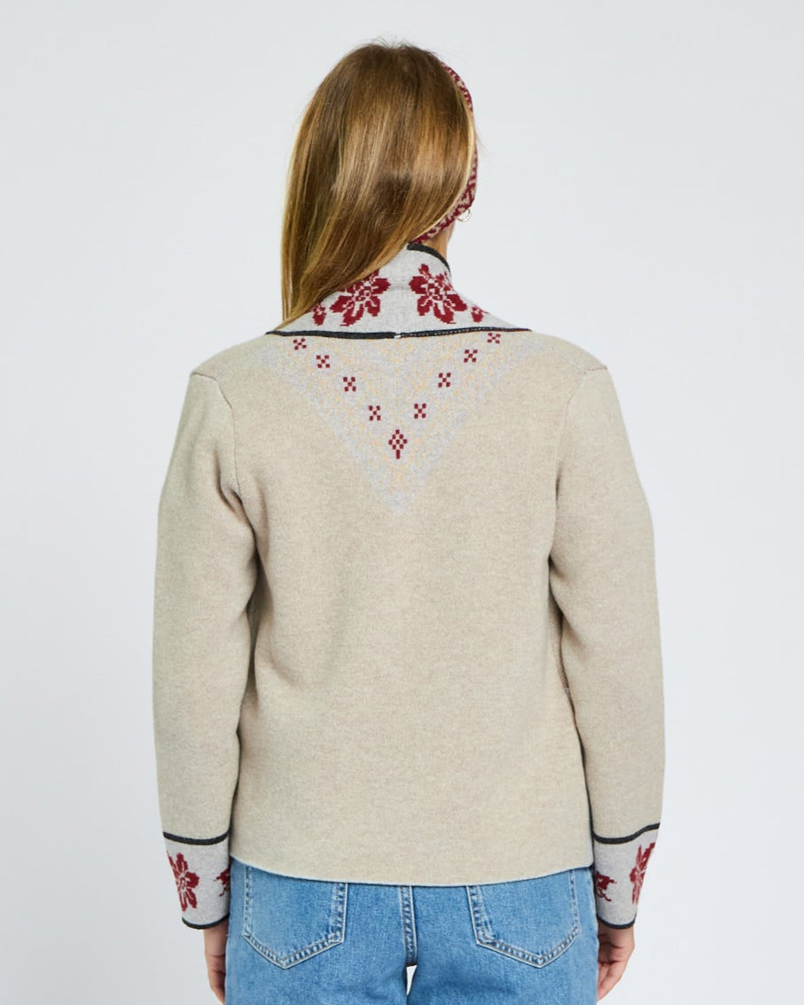 Person wearing a beige sweater with floral embroidery on a plain background