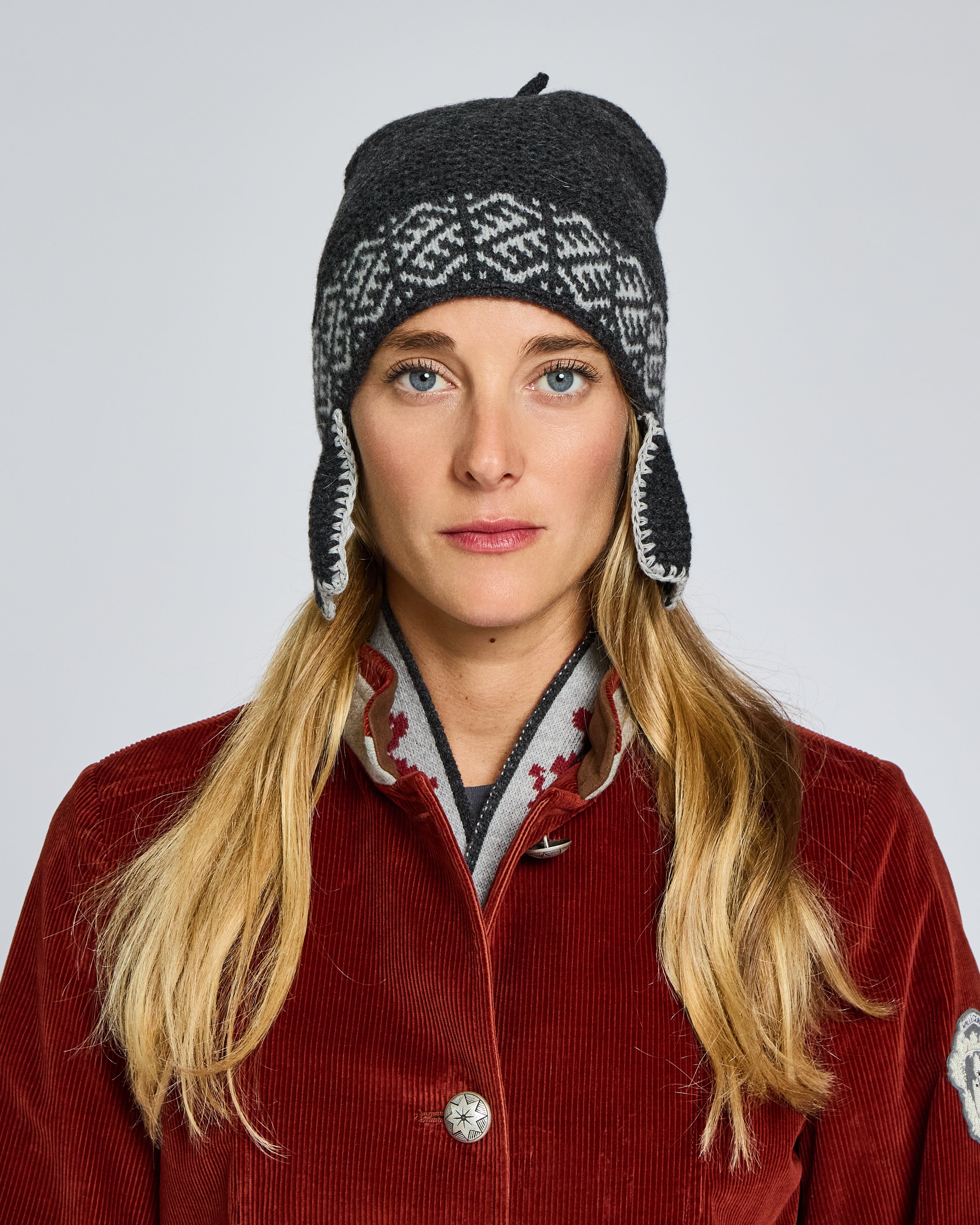 Person wearing a red coat and patterned hat on a plain background