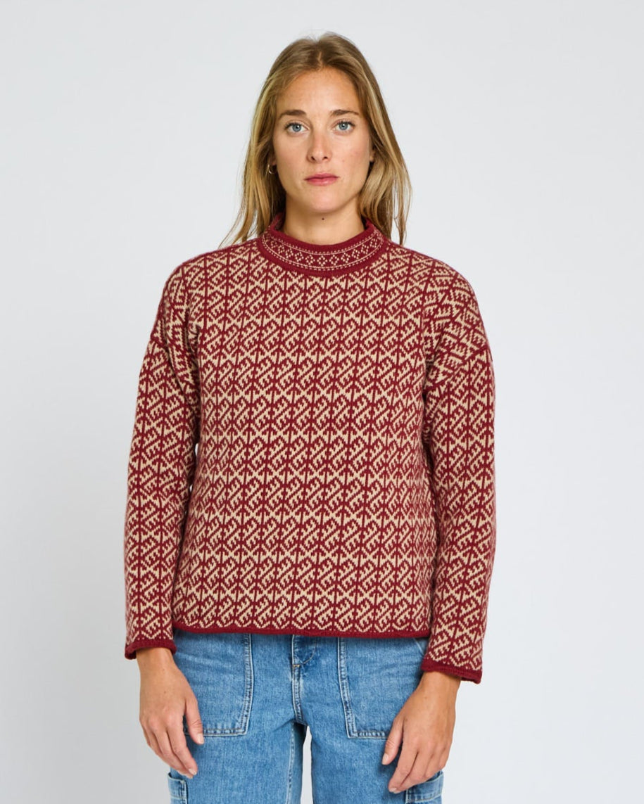 Person wearing a patterned sweater and jeans on a plain background