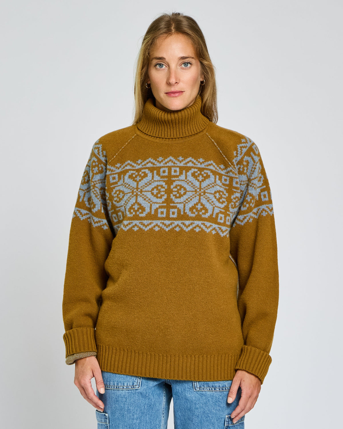 Woman wearing a mustard yellow sweater with a patterned design on a plain background