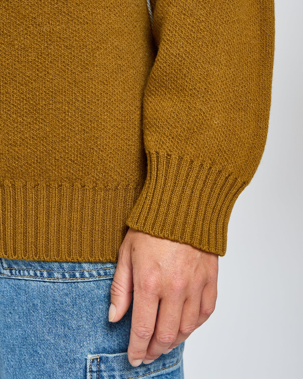 Close-up of a mustard yellow sweater and blue jeans on a plain background