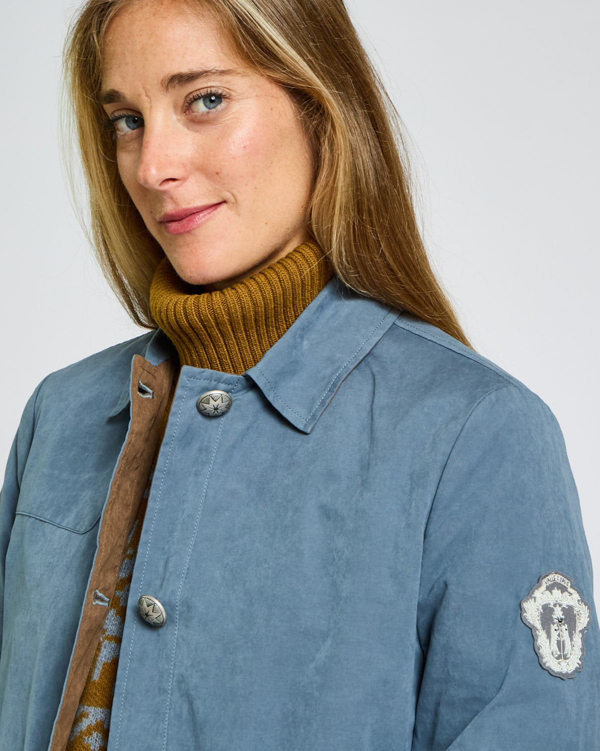 Woman wearing a blue jacket with a brand logo on a white background
