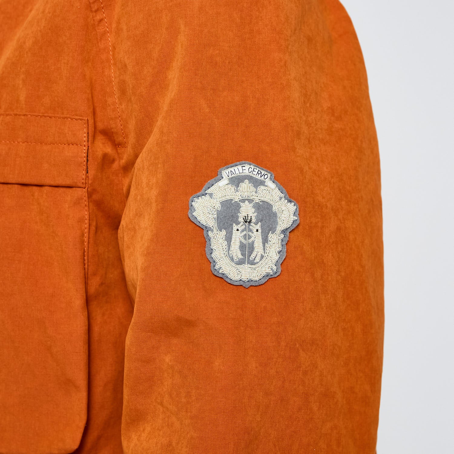 Orange jacket with a patch on the sleeve against a light gray background