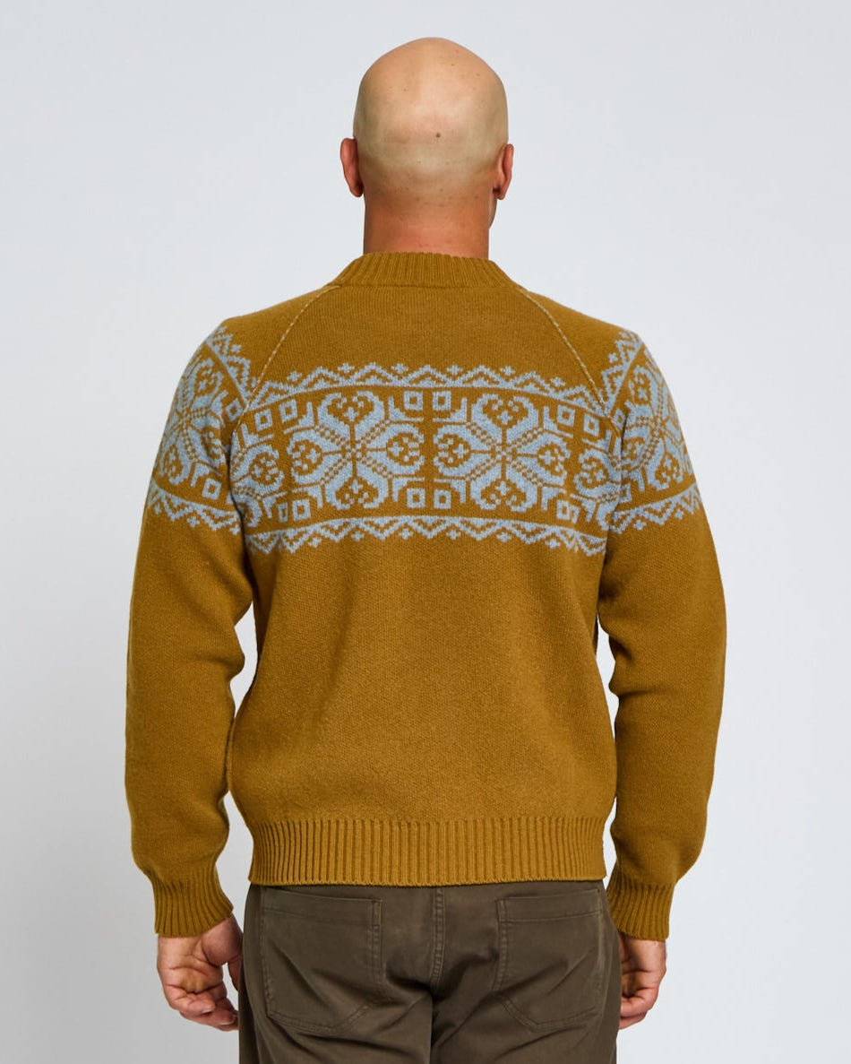 Man wearing a mustard yellow sweater with a patterned design on the back against a plain background