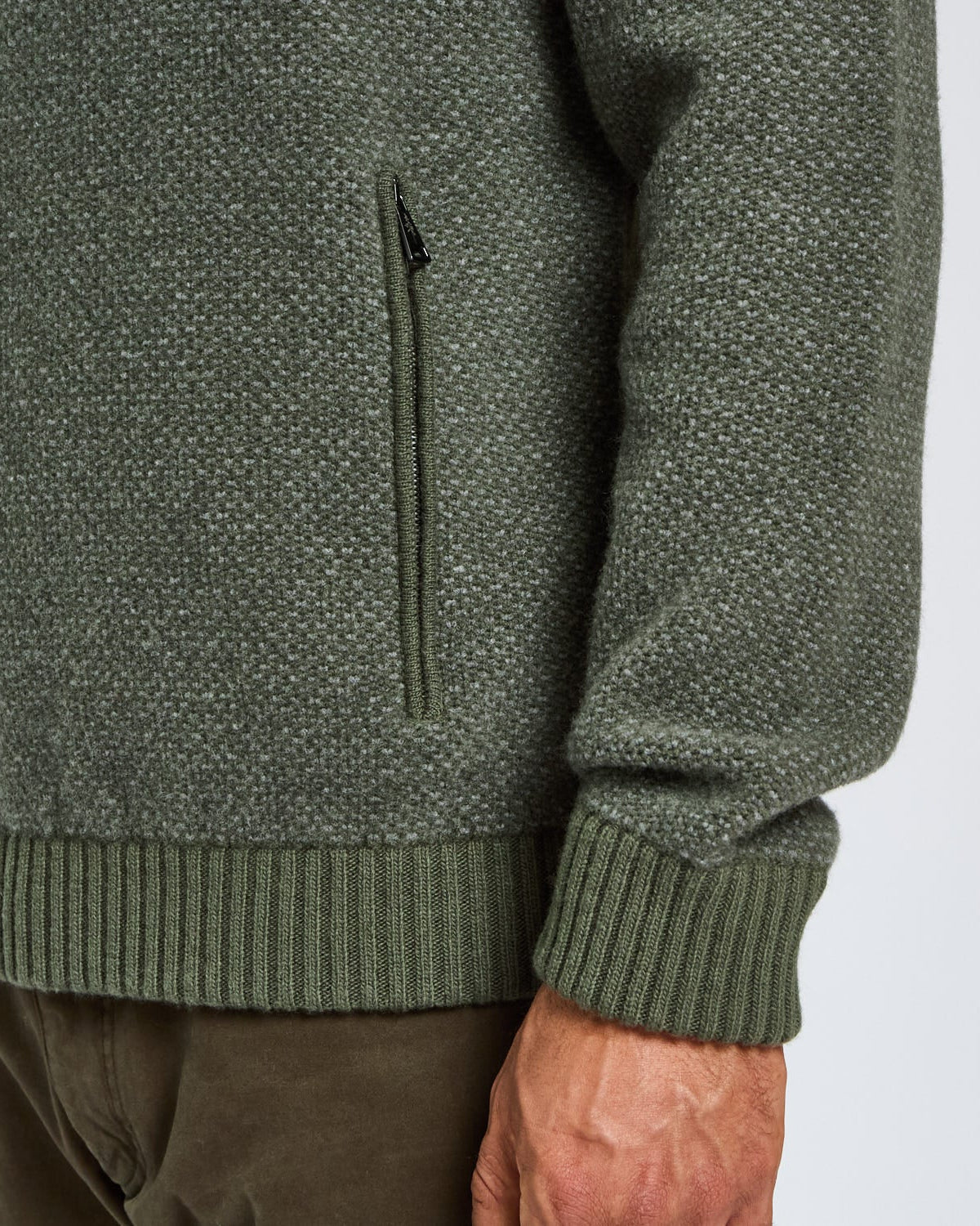 Close-up of a green knitted sweater with a pocket on a light gray background