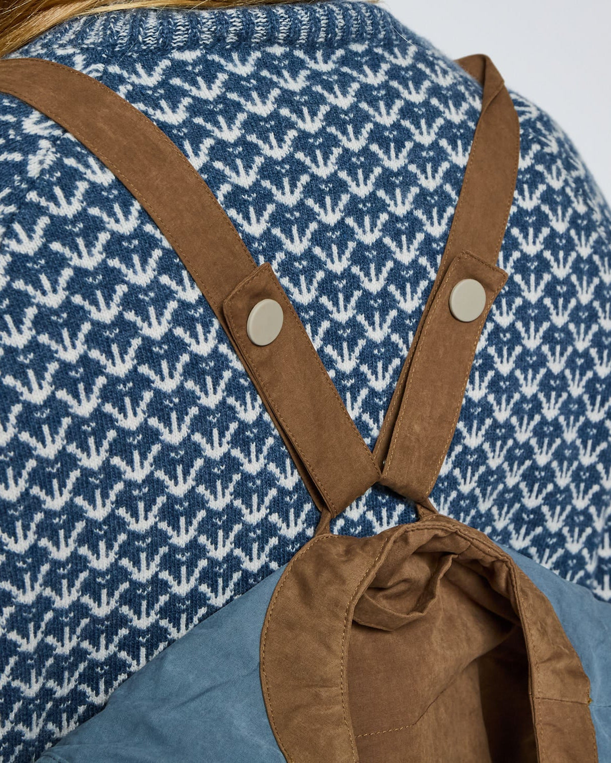 Person wearing a blue patterned shirt with brown suspenders on a white background