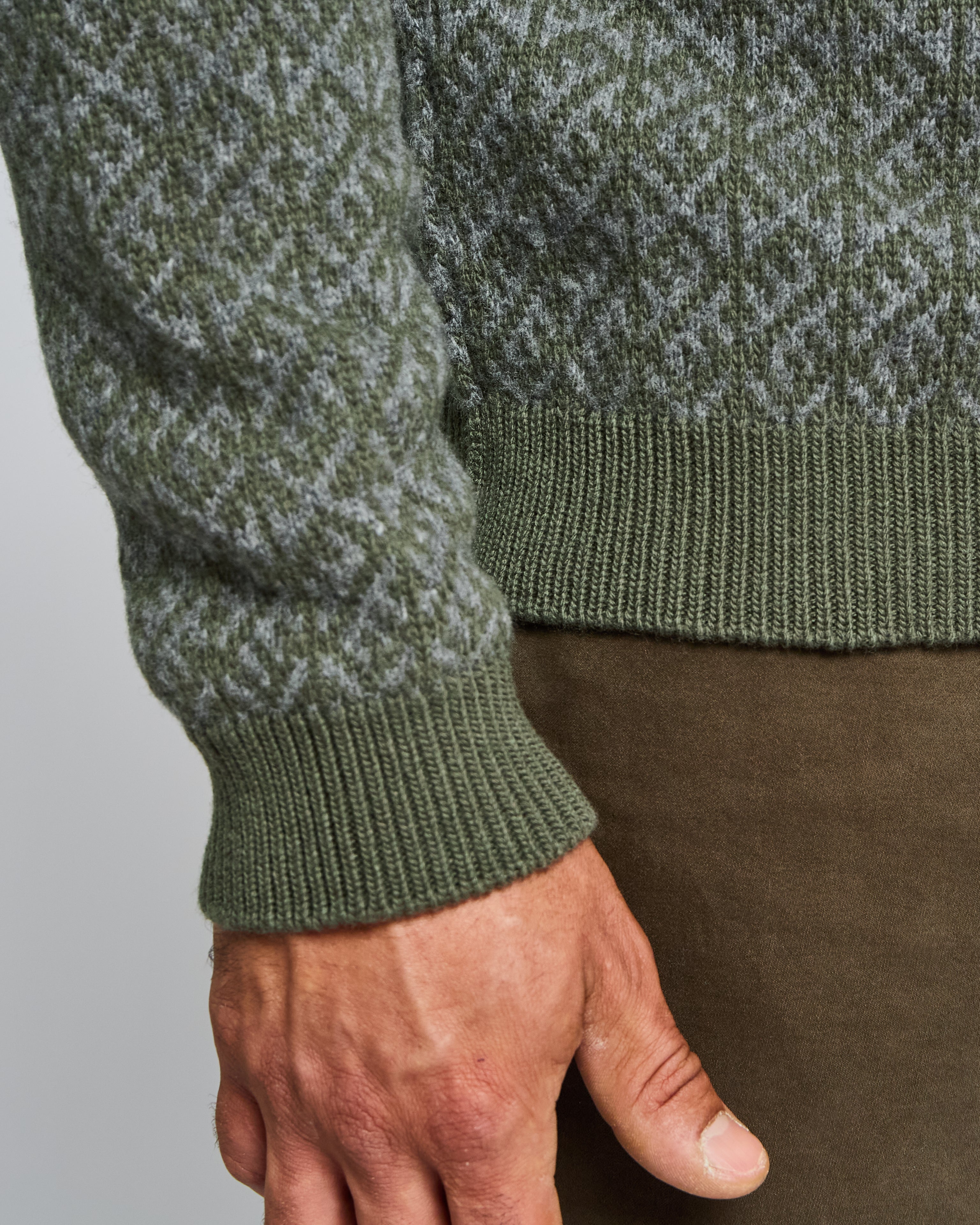 Green knitted sweater with patterned sleeves worn by a person on a plain background