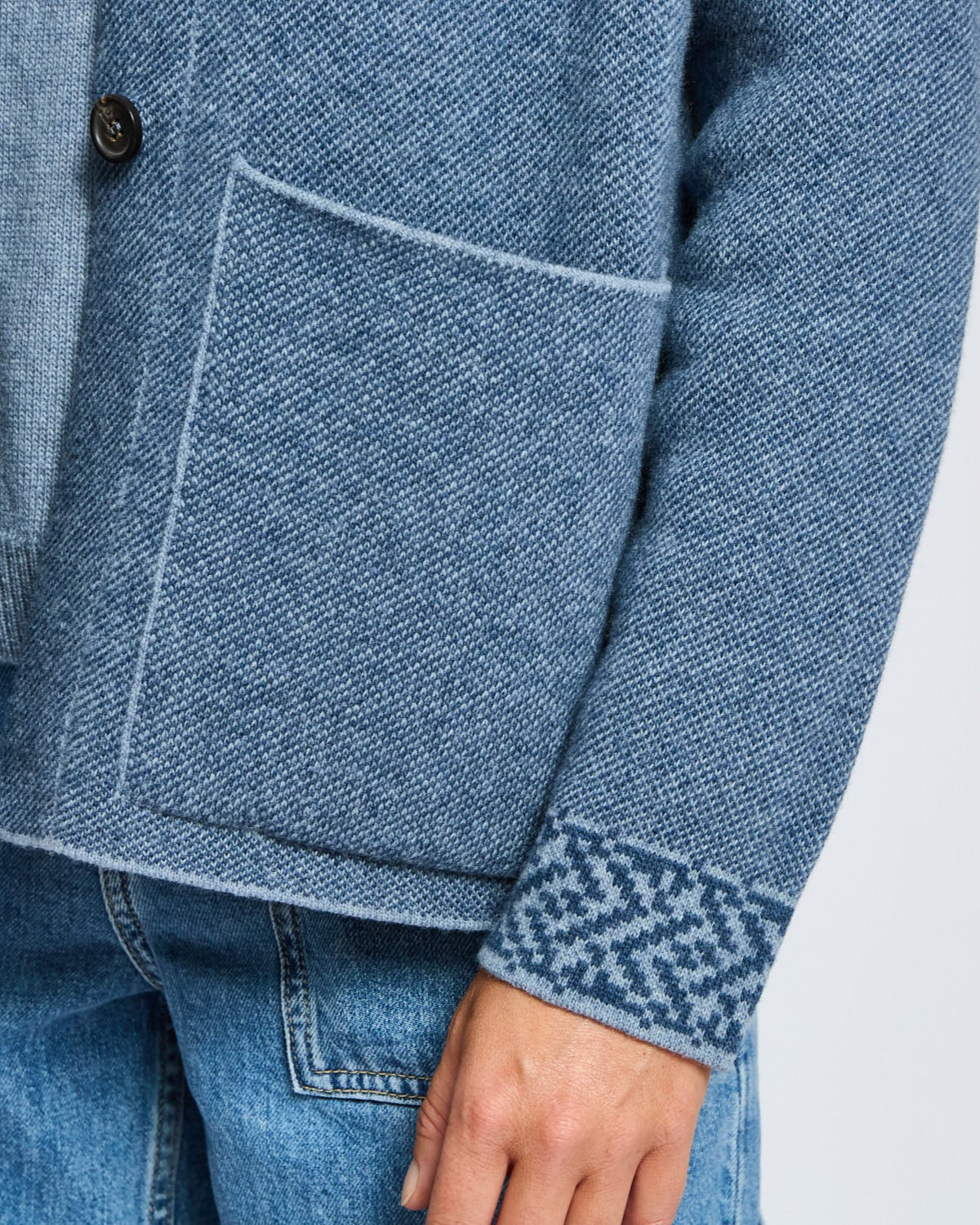 Close-up of a blue textured jacket with a pocket and matching jeans on a light gray background