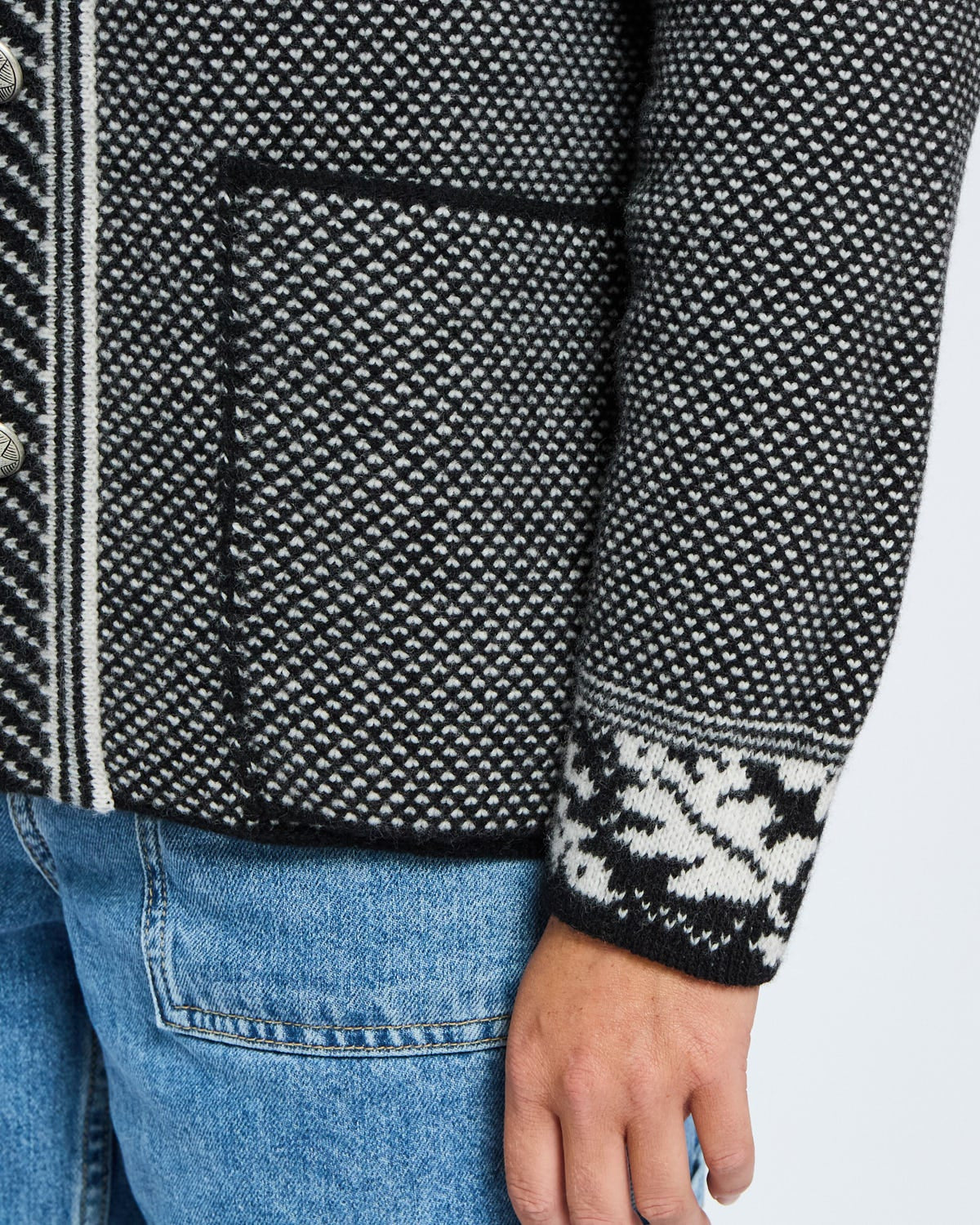 Close-up of a person wearing a black and white patterned jacket with blue jeans on a light gray background