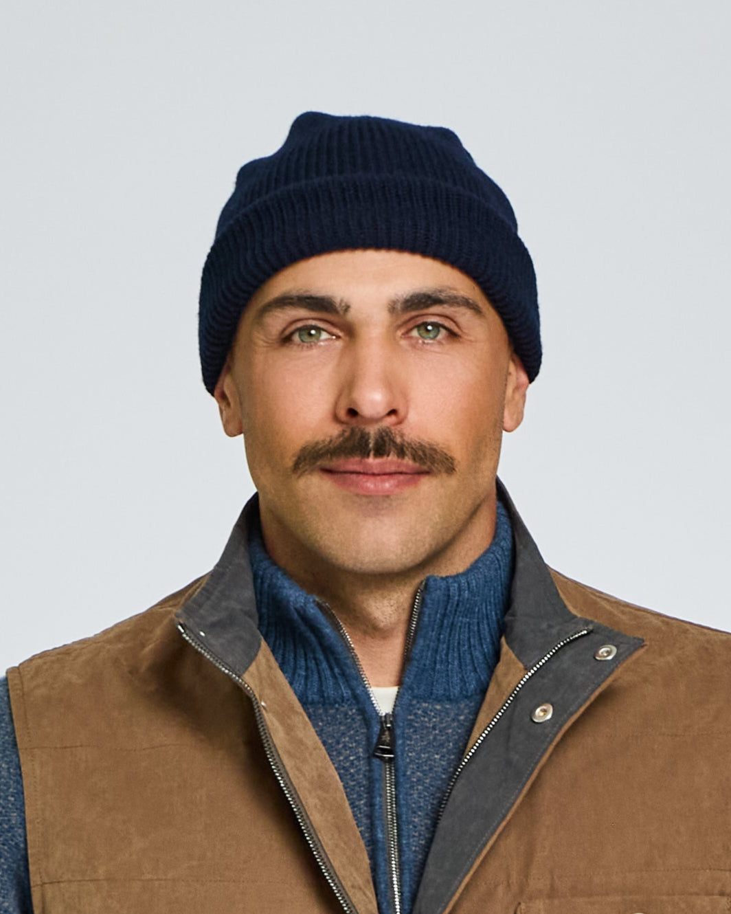 Man wearing a brown vest over a blue sweater with a white background