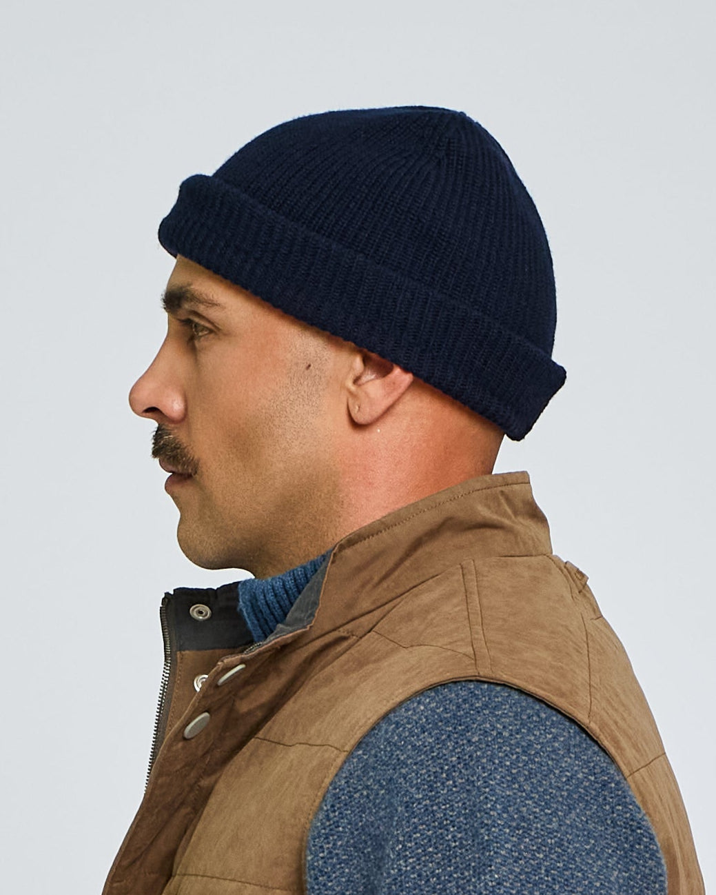 Man wearing a brown vest over a blue sweater on a light gray background