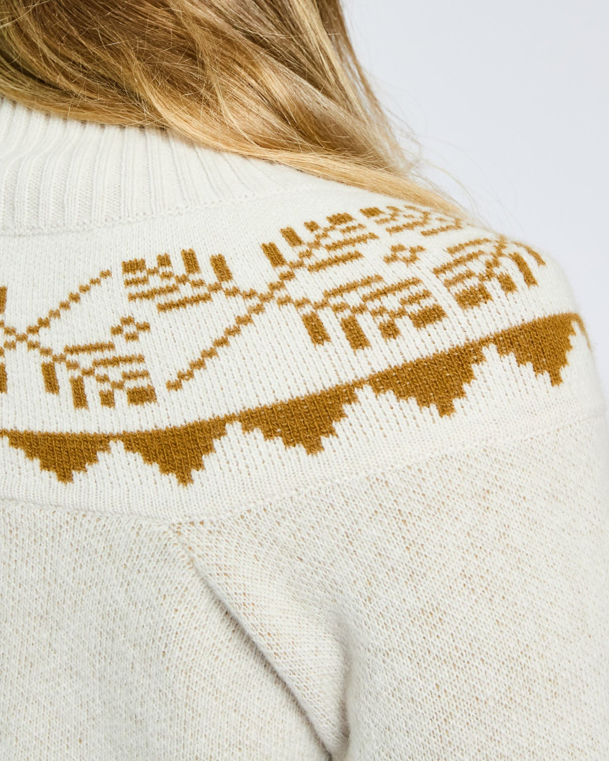 Close-up of a white sweater with brown pattern on a plain background