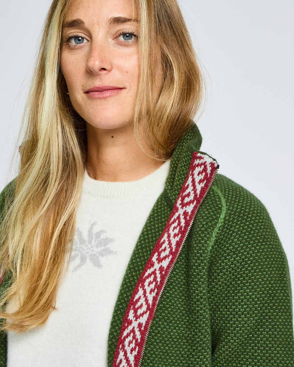 Woman wearing a green cardigan with a red and white patterned strap over her shoulder on a light gray background
