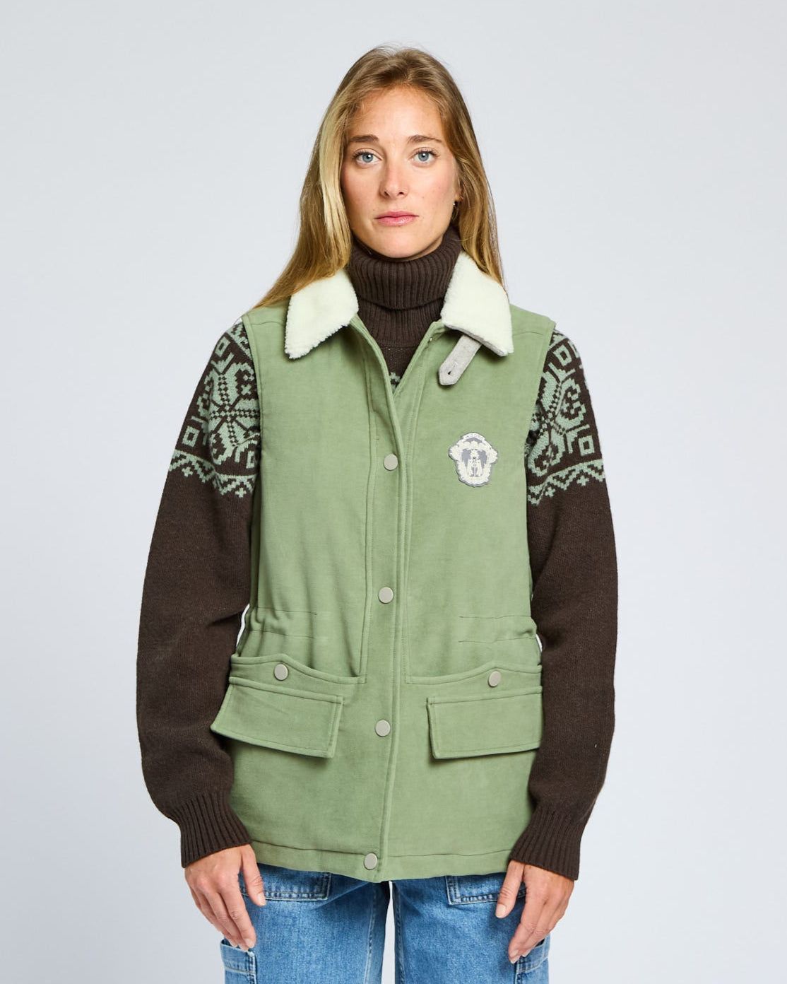 Person wearing a green and brown jacket with patterned sleeves on a light gray background