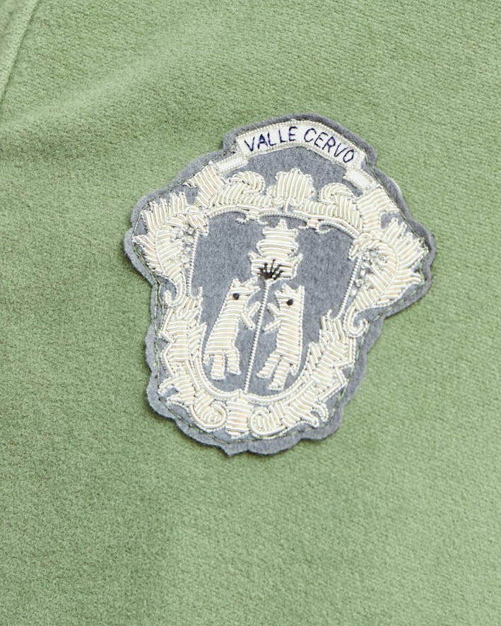 Green jacket with a embroidered patch featuring two figures and text on a green background