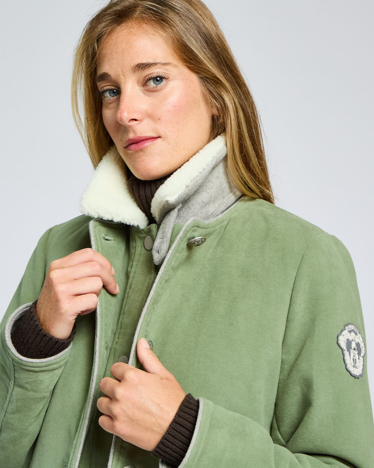 Woman wearing a green coat with a white collar against a light gray background