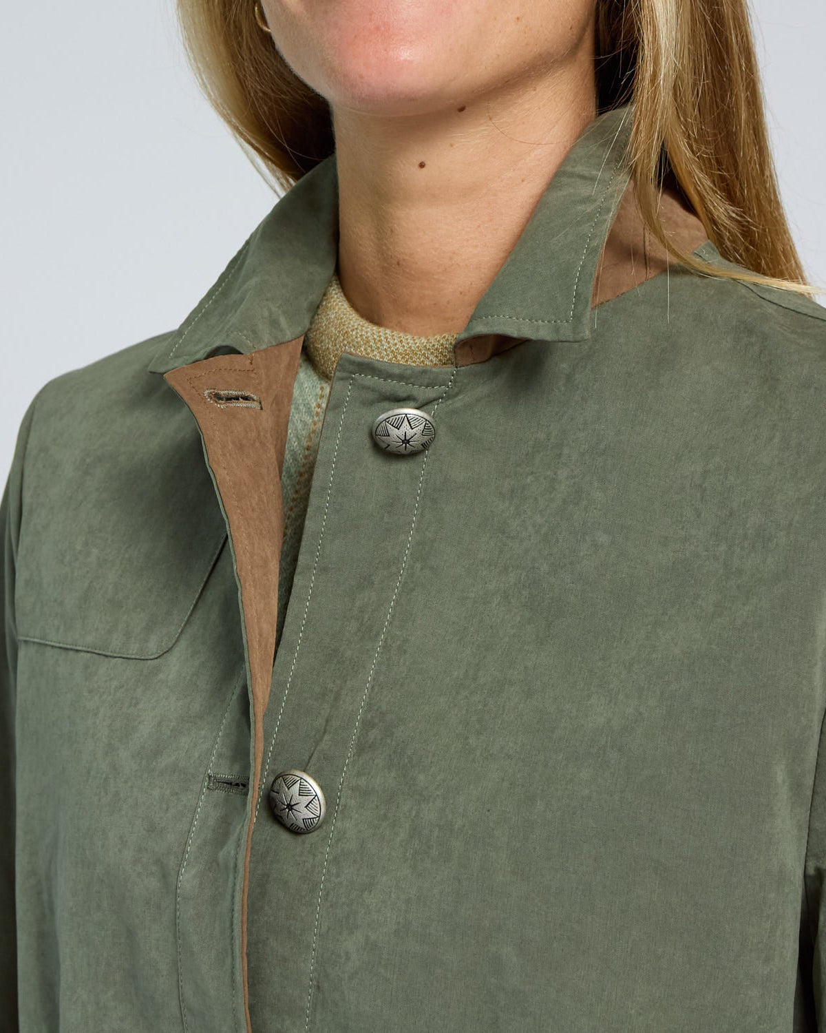 Close-up of a person wearing a green jacket with a button detail on a light gray background