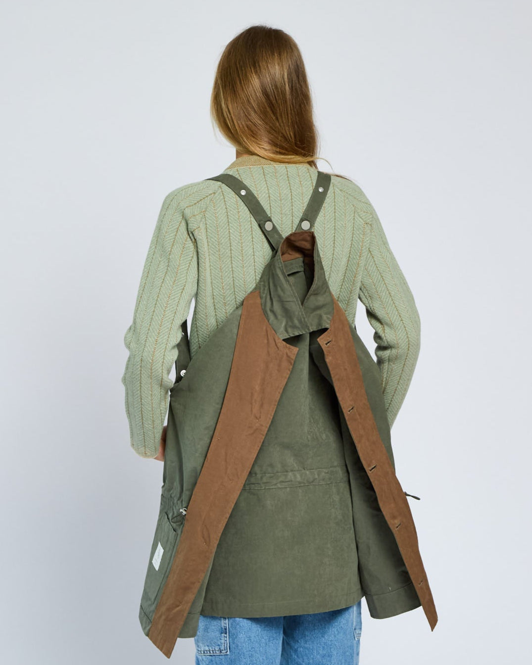 Person wearing a green jacket with a brown apron over a white background