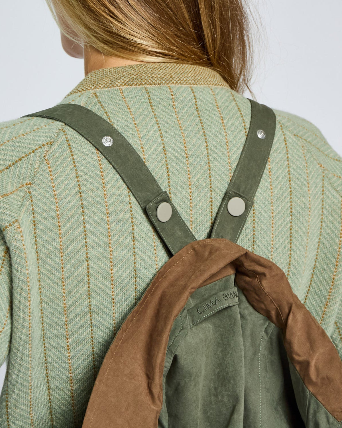 Person wearing a green textured jacket with brown overalls on a light gray background