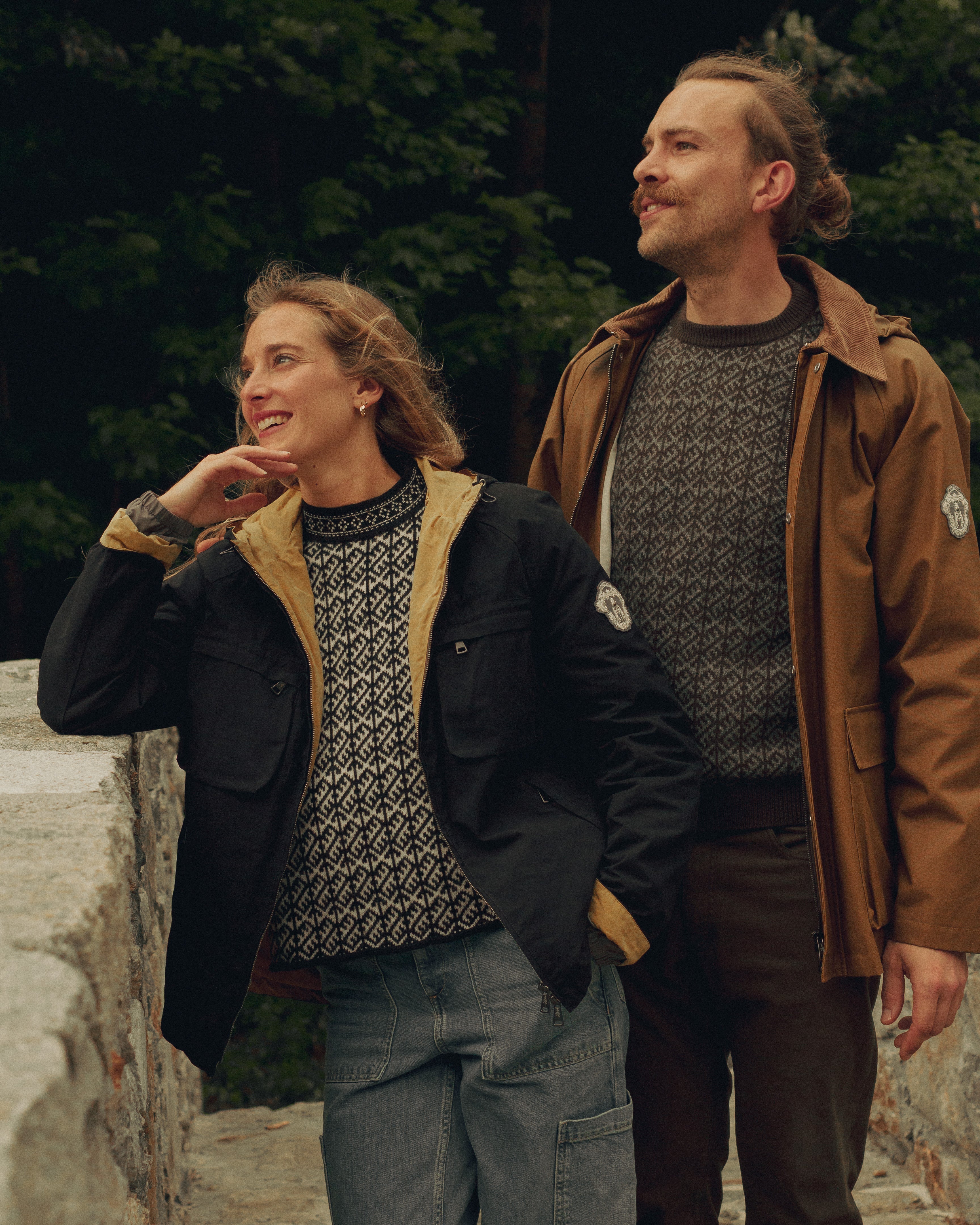 Two people standing outdoors, wearing patterned sweaters and jackets.