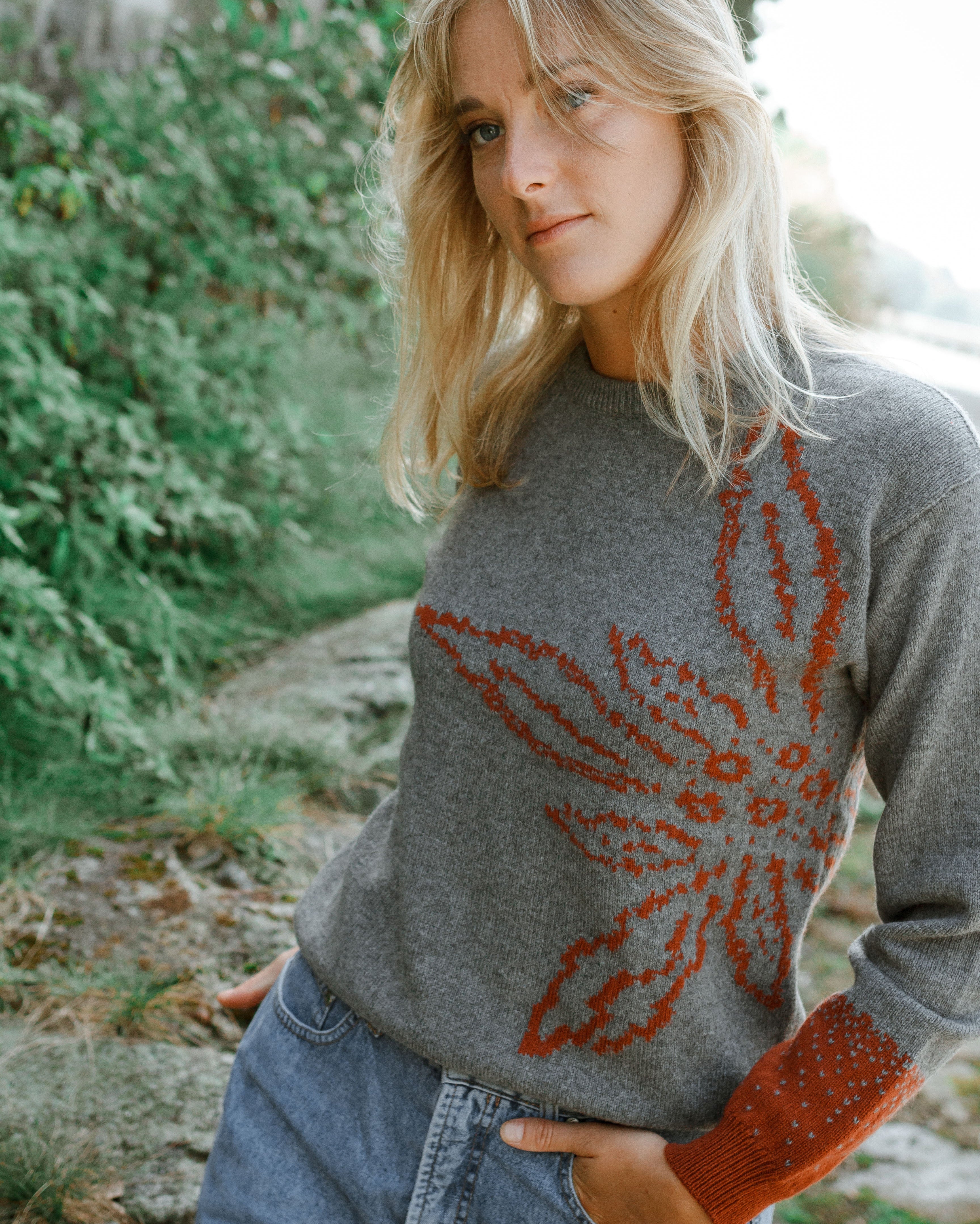 Woman wearing a gray sweater with a red floral pattern outdoors.