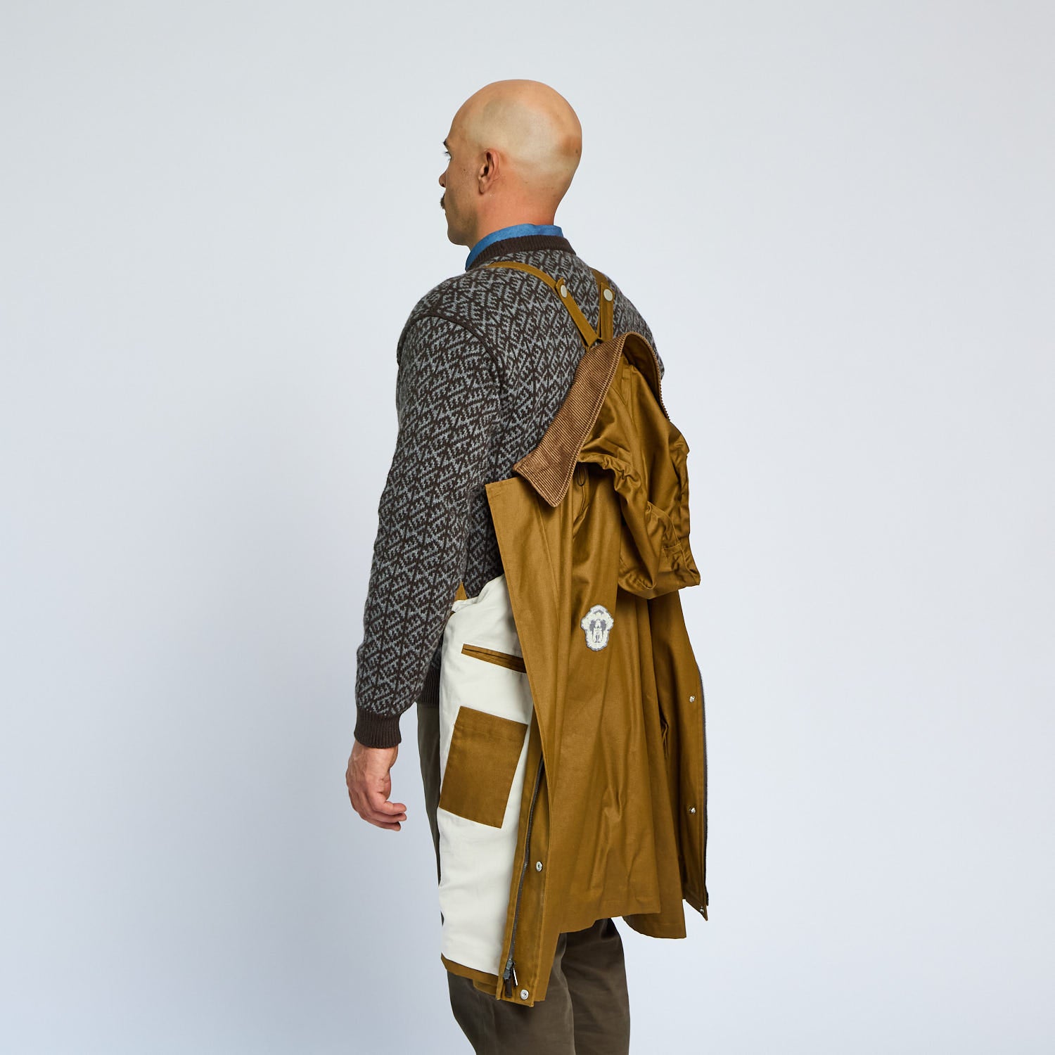 Person wearing a brown jacket over a patterned shirt on a plain background
