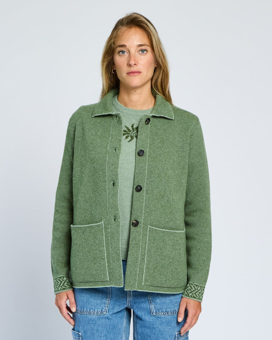 Person wearing a green jacket and blue jeans on a plain background