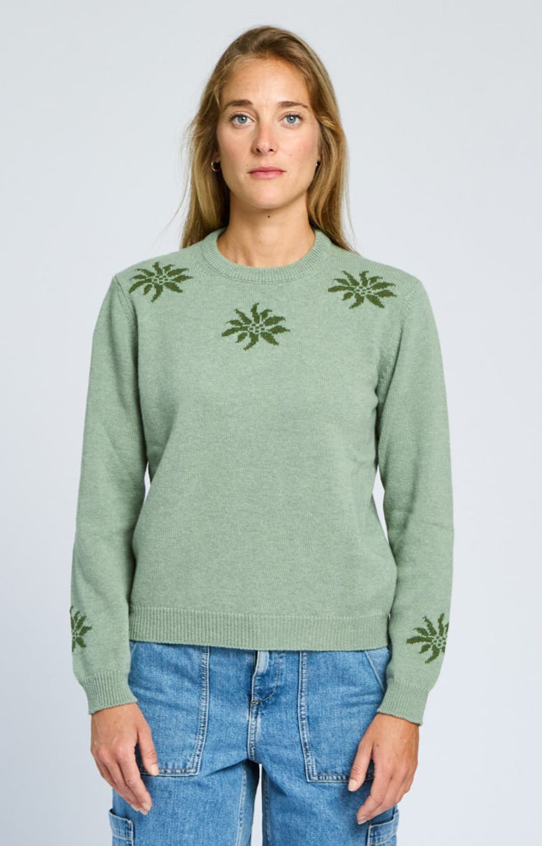 Woman wearing a green sweater with floral patterns on a light gray background