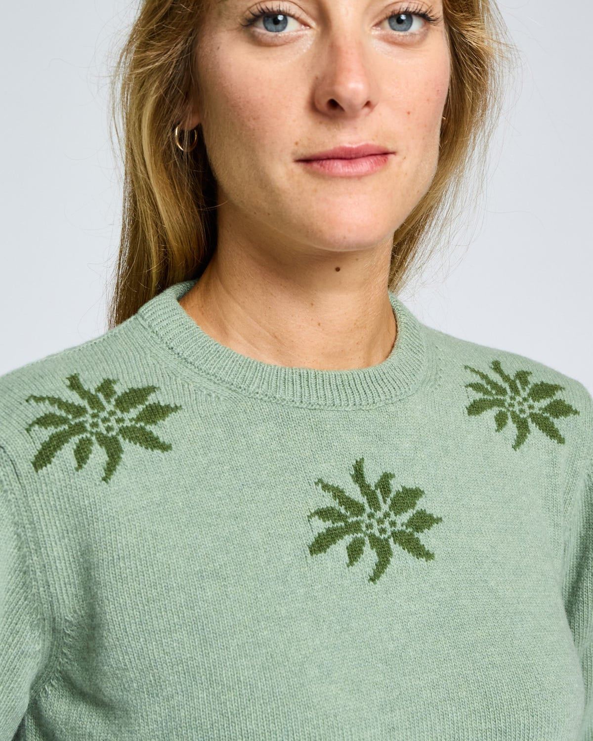 Woman wearing a green sweater with floral patterns on a plain background