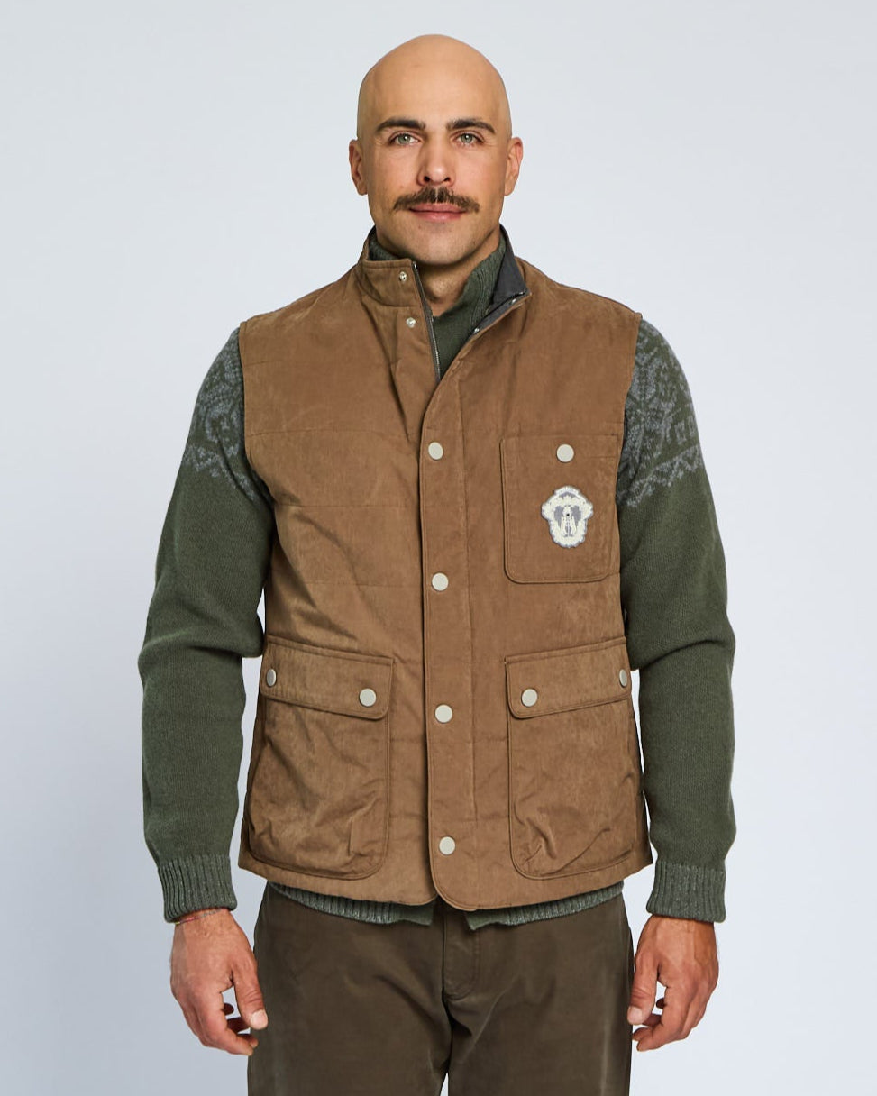 Man wearing a brown vest over a green shirt on a light gray background