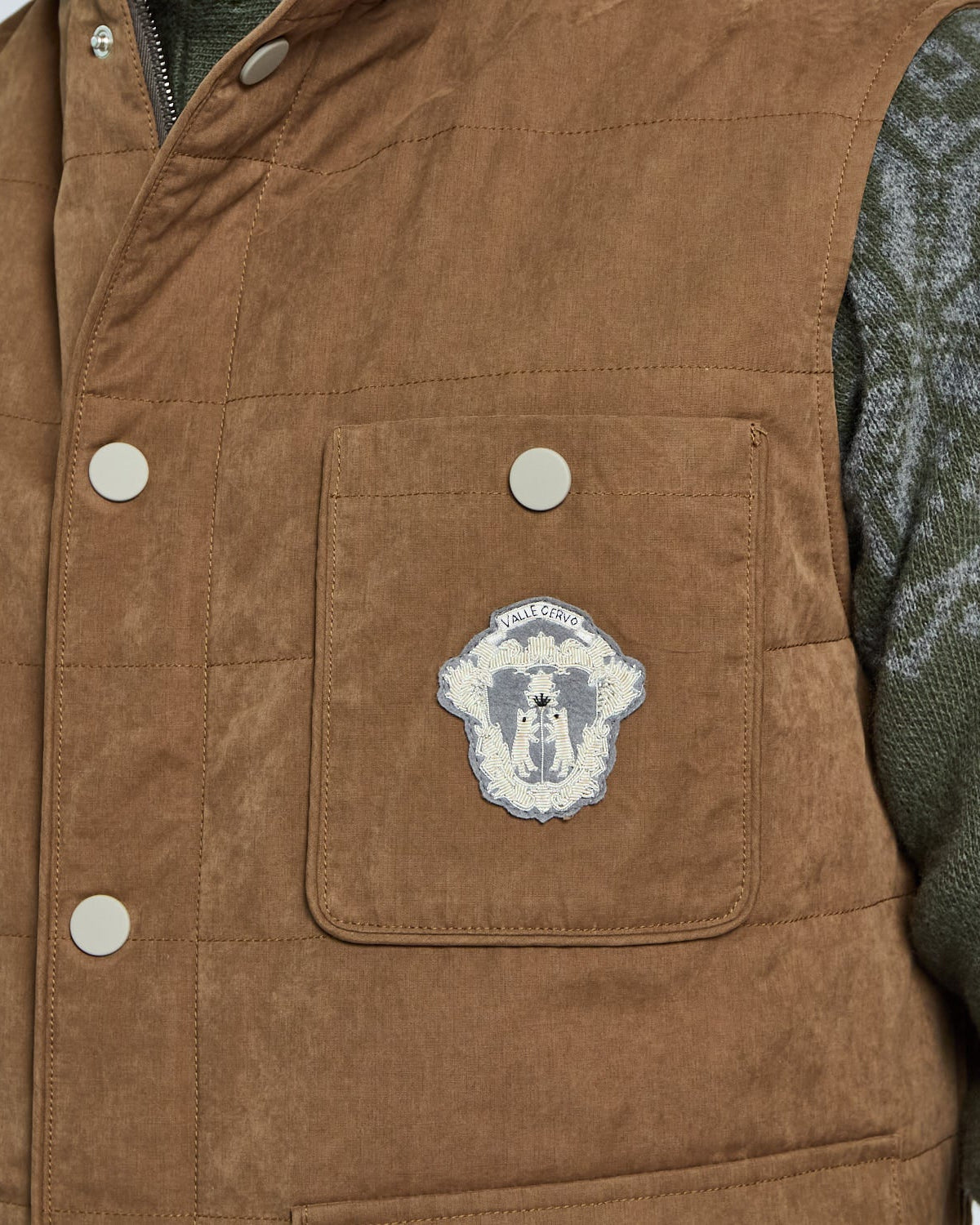 Brown vest with a patch on the chest, worn over a green sweater.