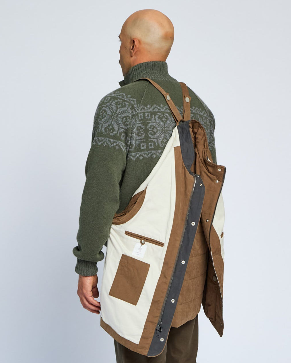 Man wearing a green patterned sweater and brown apron over a white background