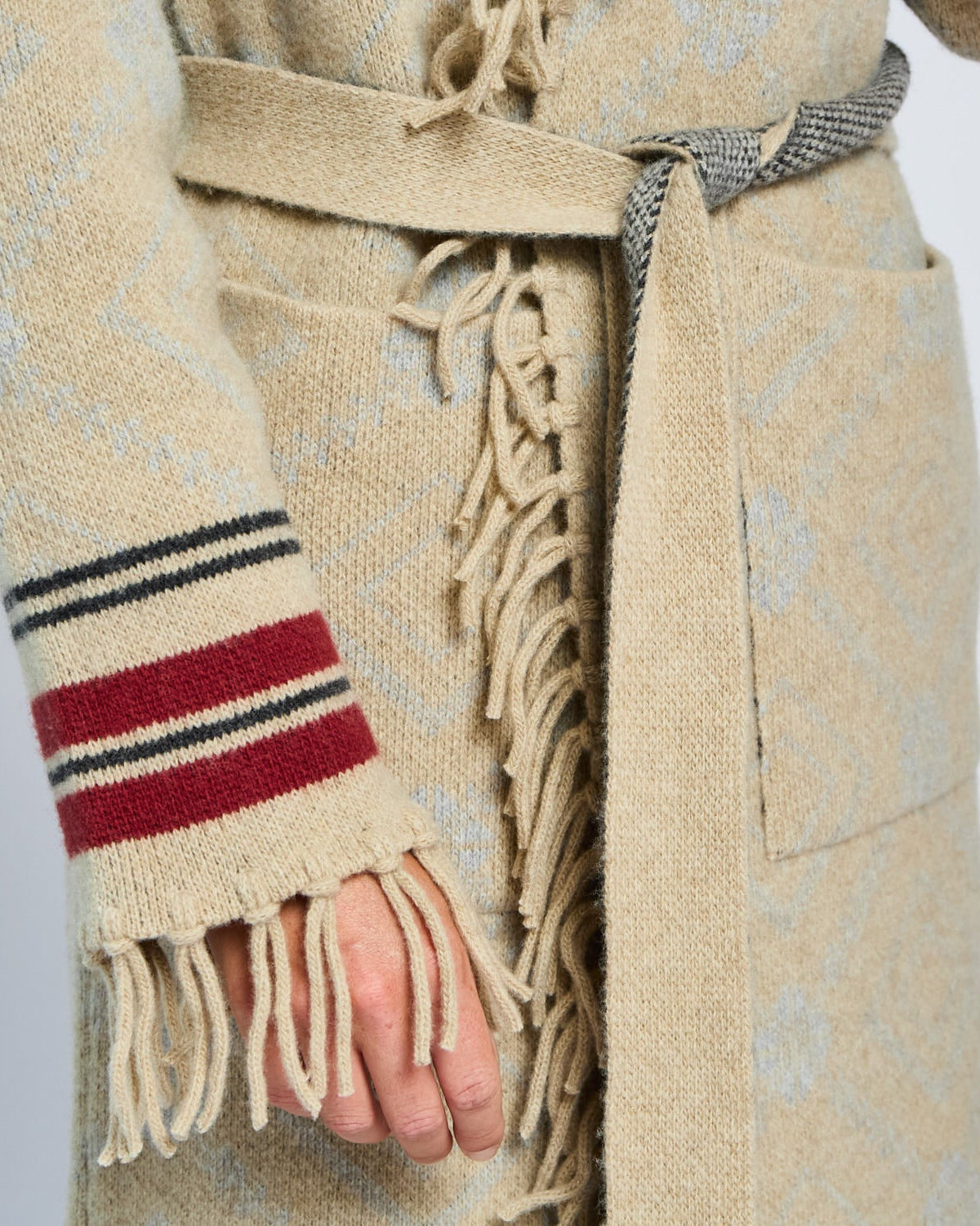 Beige coat with fringed scarf and striped sleeve on a plain background