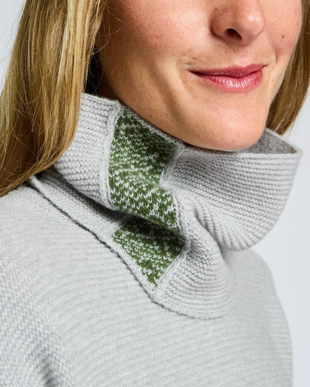 Person wearing a gray knitted scarf with green pattern on a white background