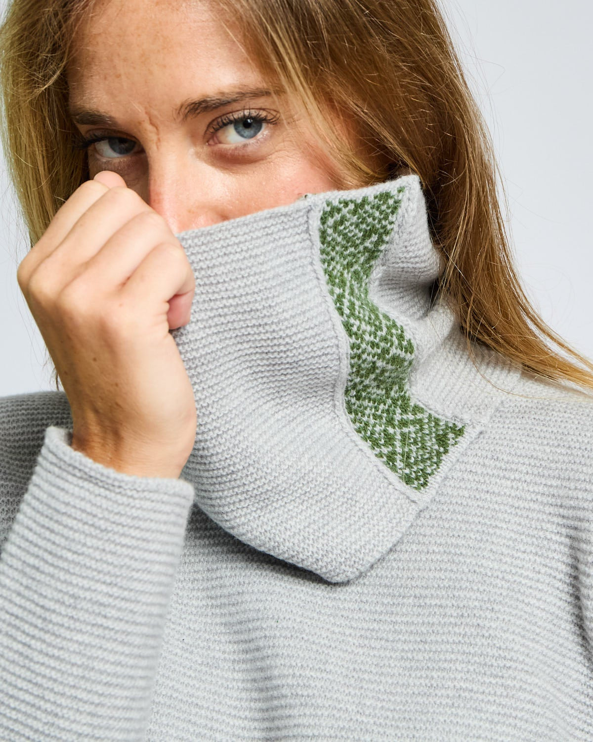 Woman wearing a gray sweater with a green patterned turtleneck