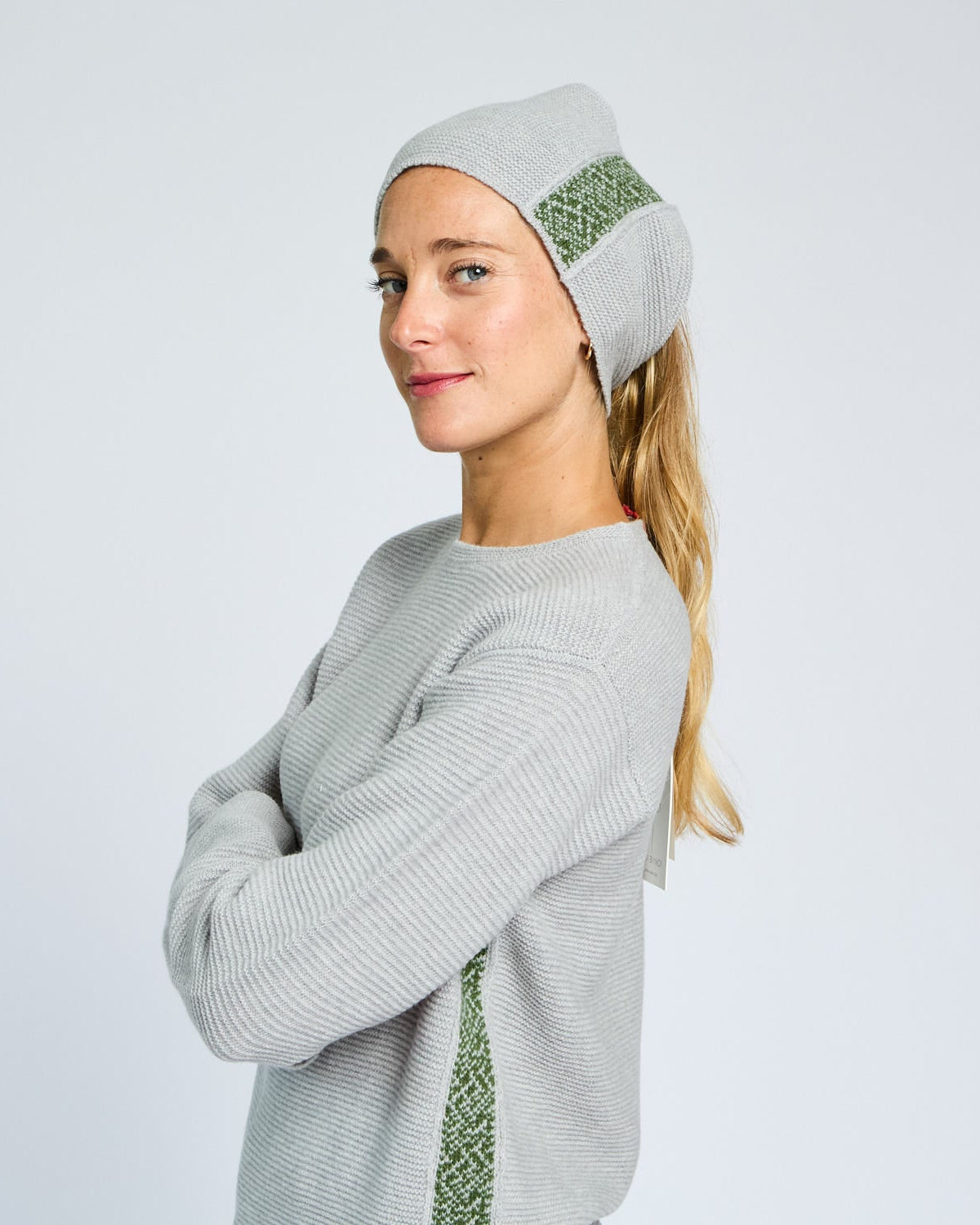Woman wearing a gray knit beanie with green pattern and matching sweater on a light gray background