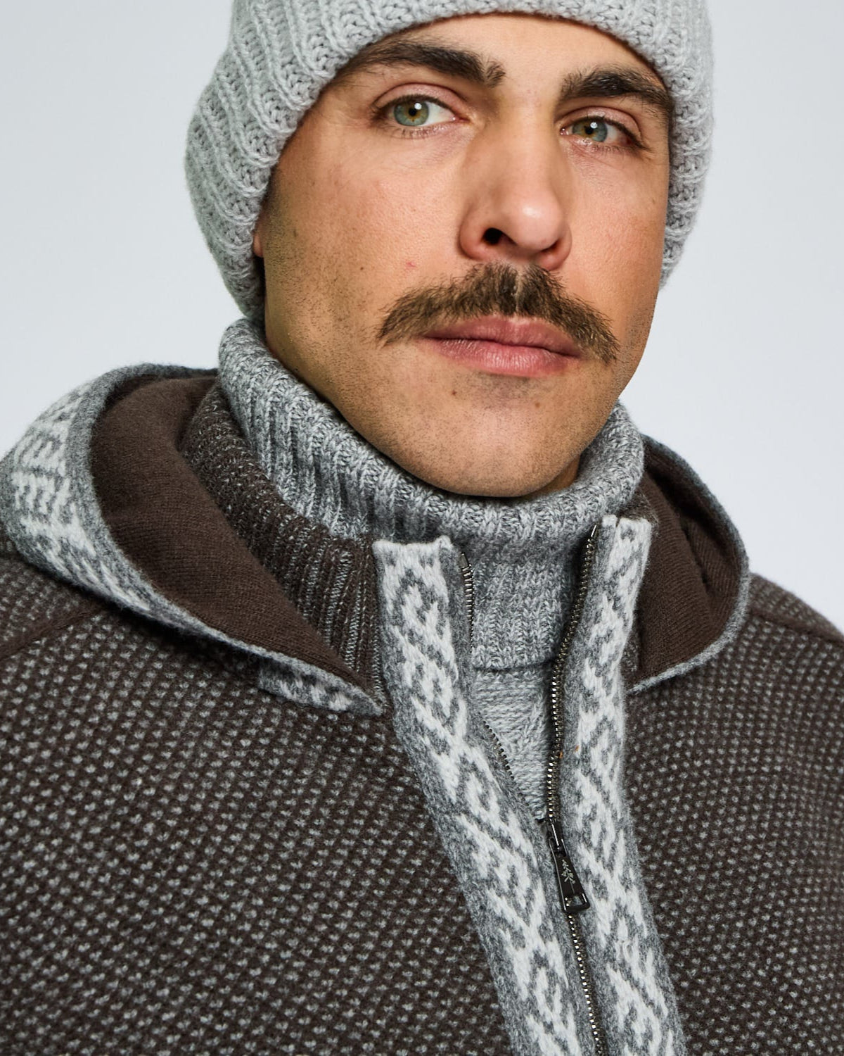 Man wearing a gray knit beanie and patterned jacket on a light gray background