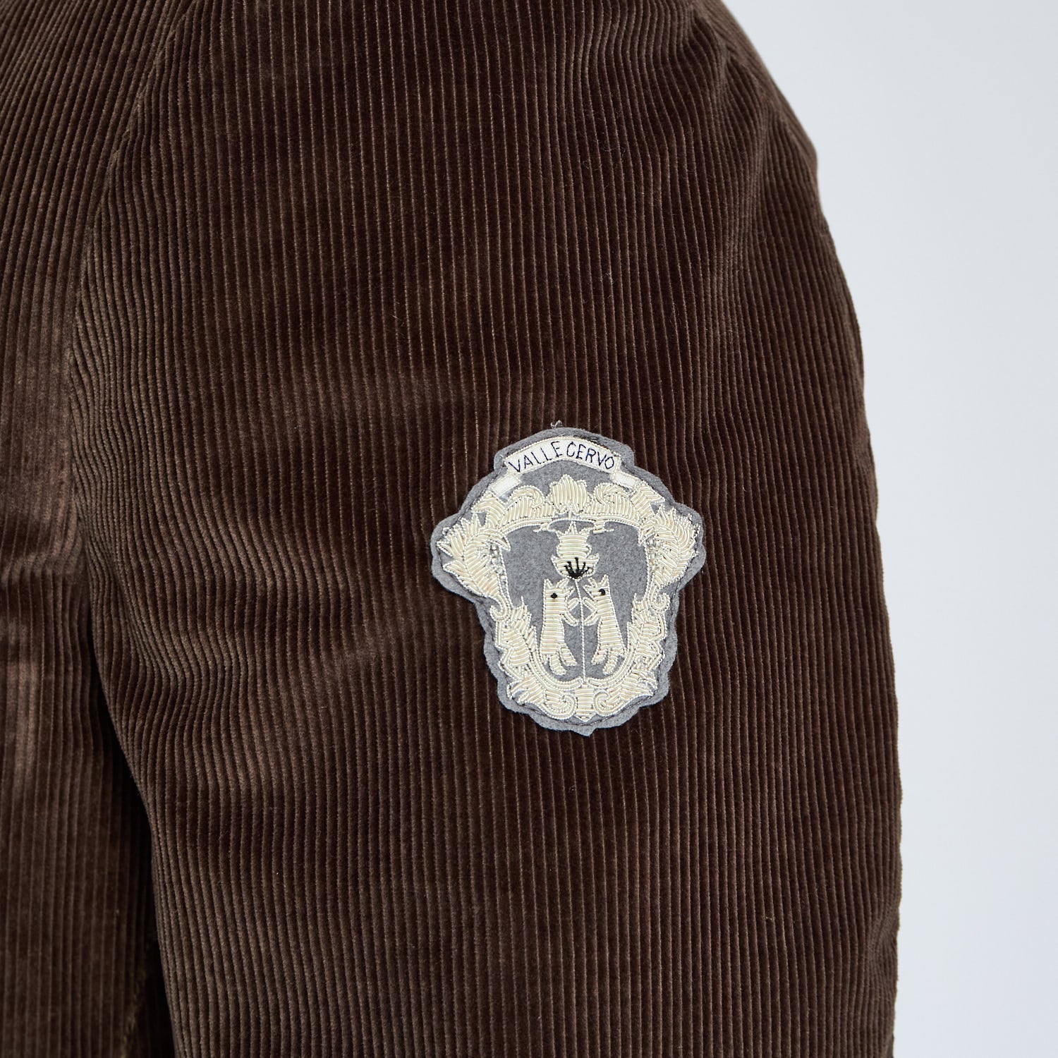 Brown corduroy jacket with a decorative patch on a light gray background