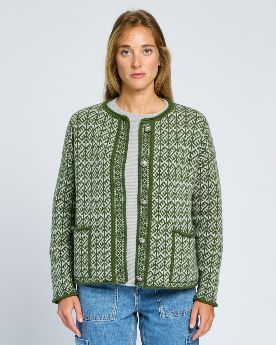 Woman wearing a green patterned cardigan and blue jeans on a light gray background