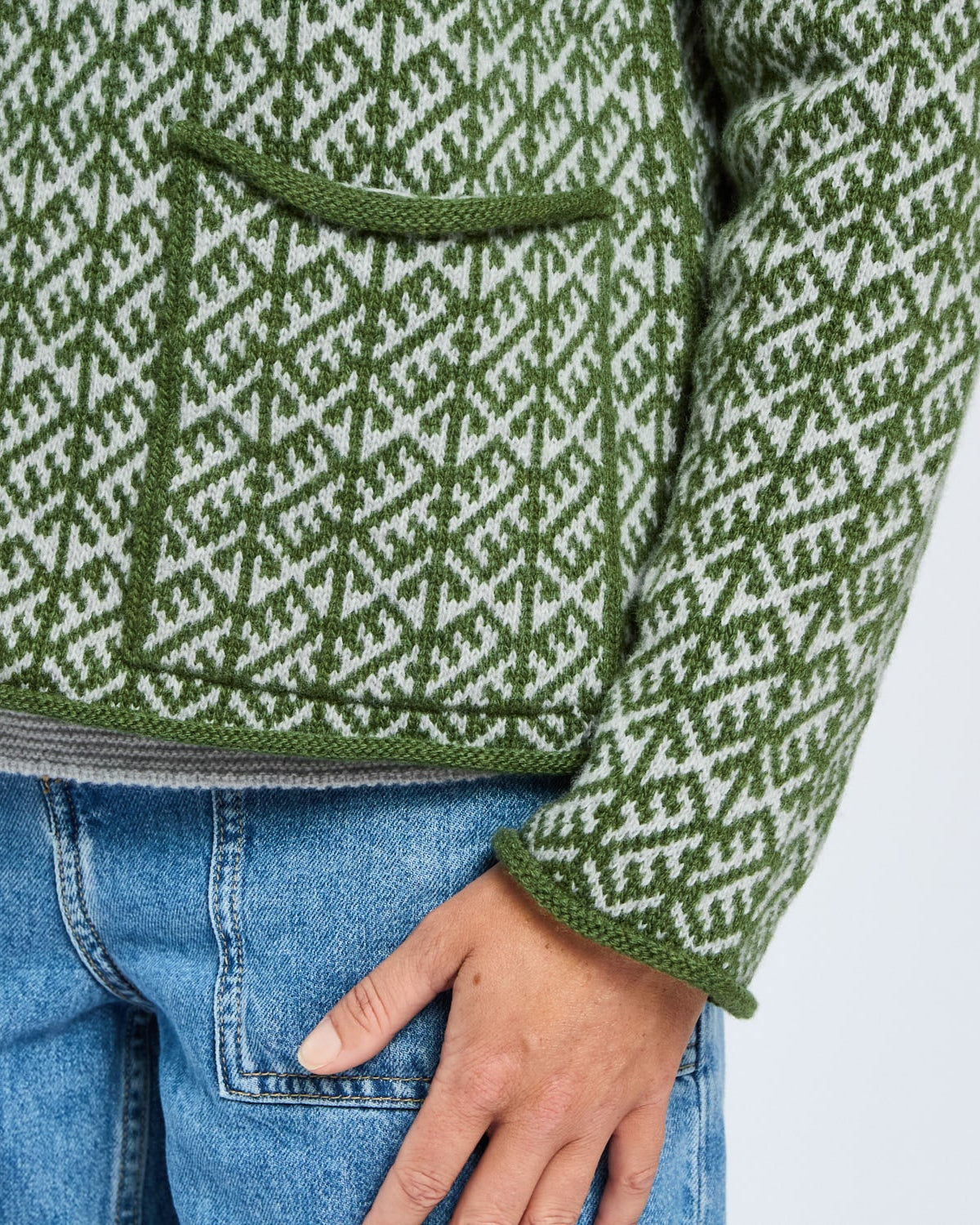 Green and white patterned sweater with a pocket on a plain background
