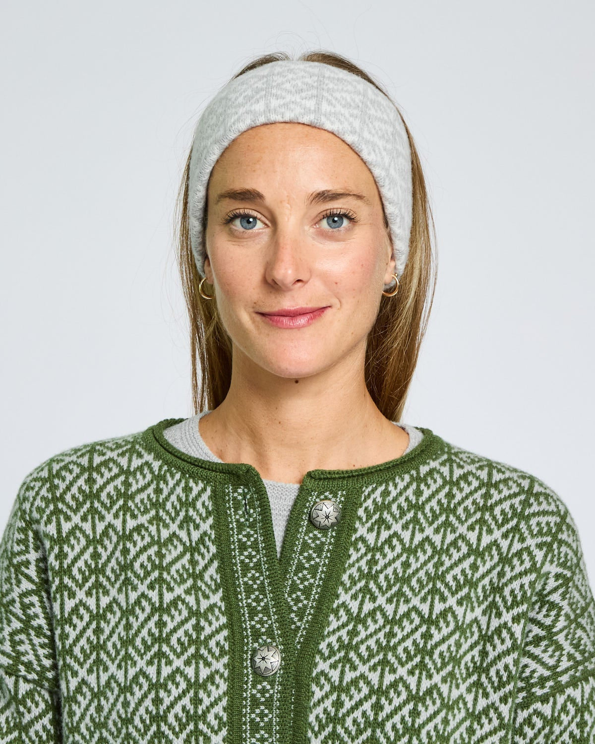 Woman wearing a green patterned cardigan and white headband against a light gray background