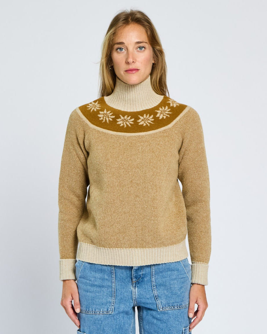Woman wearing a beige sweater with a patterned design on a plain background