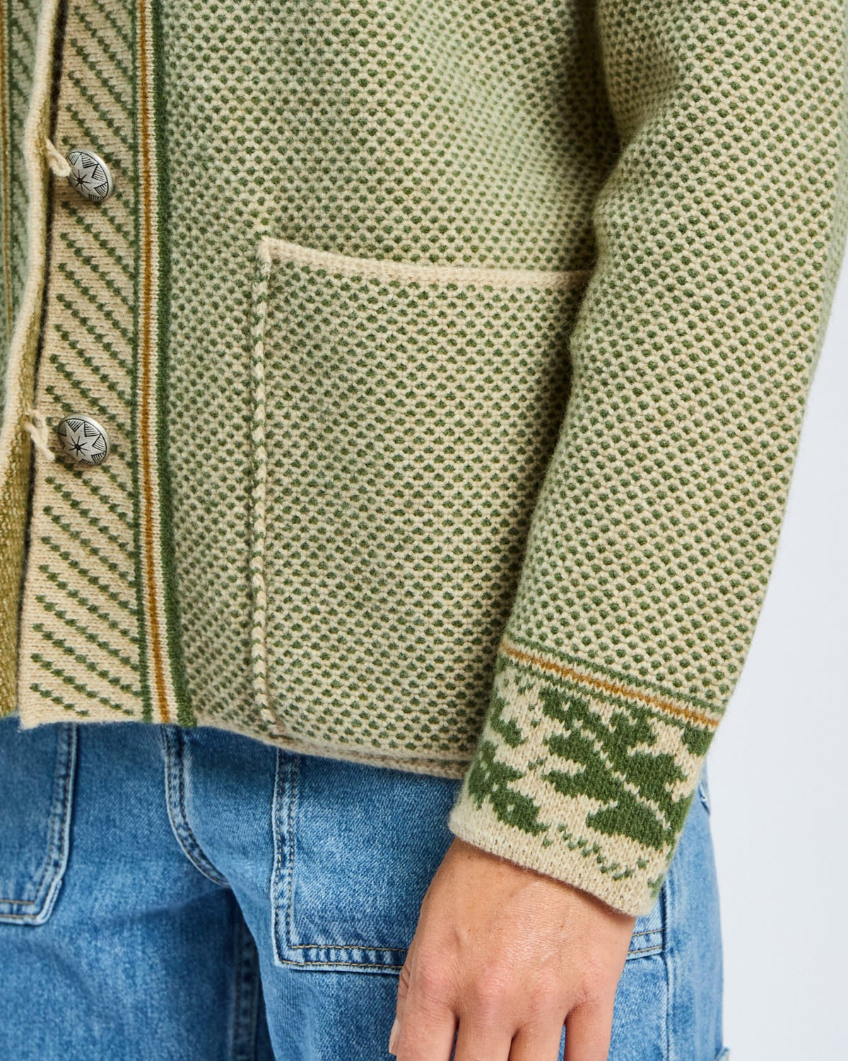 Green patterned jacket with blue jeans on a plain background